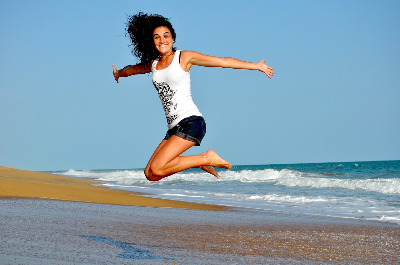 Smiling woman jumping on a beach illustrating health and wellbeing.